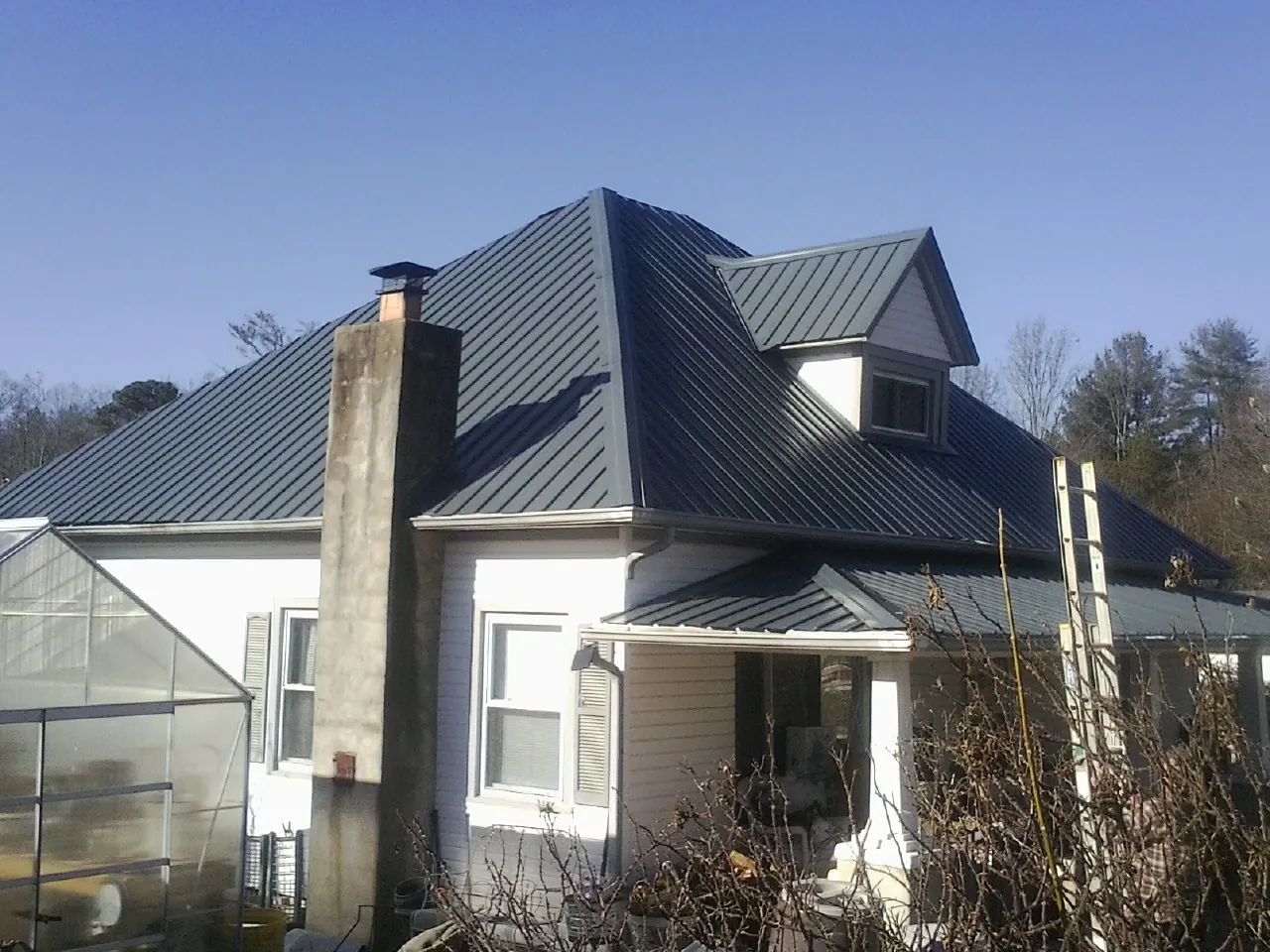 Dark blue standing seam metal roof on a white farmhouse with dormer — Slate & Tile Roof Repair by Roofing Brothers in Saint Ann