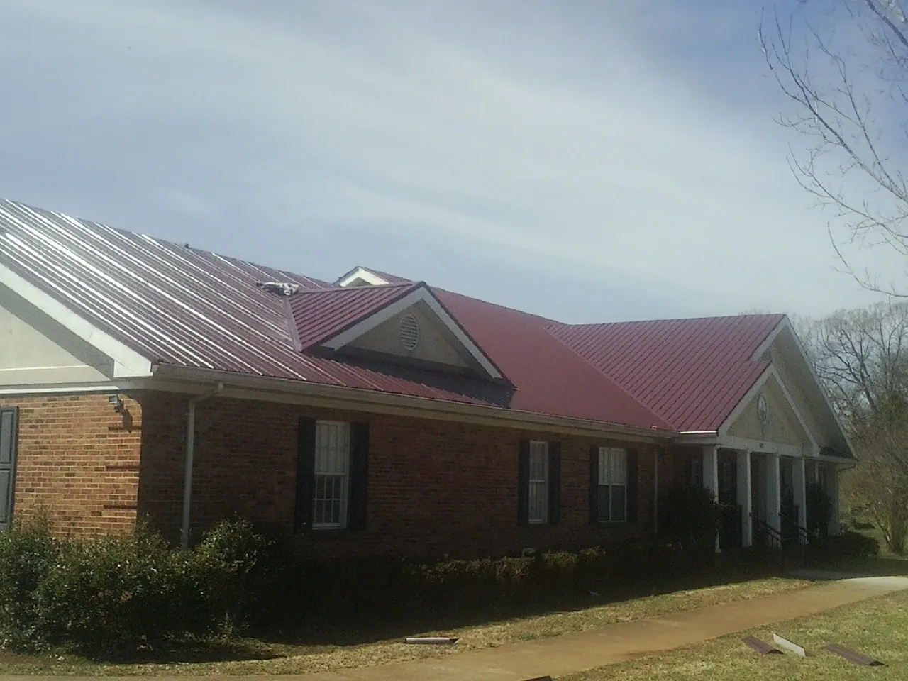 Red metal roof with gabled entries on a long brick building, from a Hail Damage Roof Repair job in Saint Ann