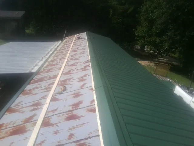 Old rusted panels beside newly installed green metal roofing — Wind Damage Roof Repair by Roofing Brothers in Saint Ann