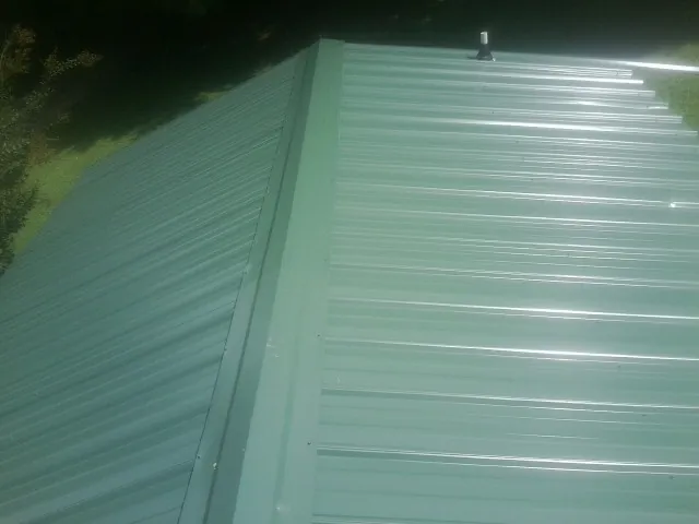 New green metal panels meeting at the ridge of a roof — Flat Roof Repair work by our crew in Saint Ann