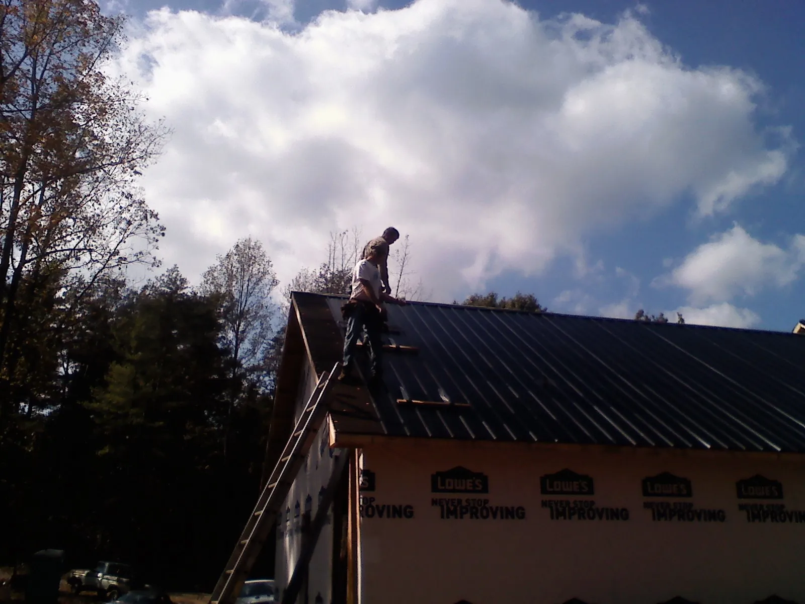Roofer fastening dark metal panels high against a cloudy sky, from a Roof Inspection job in Saint Ann