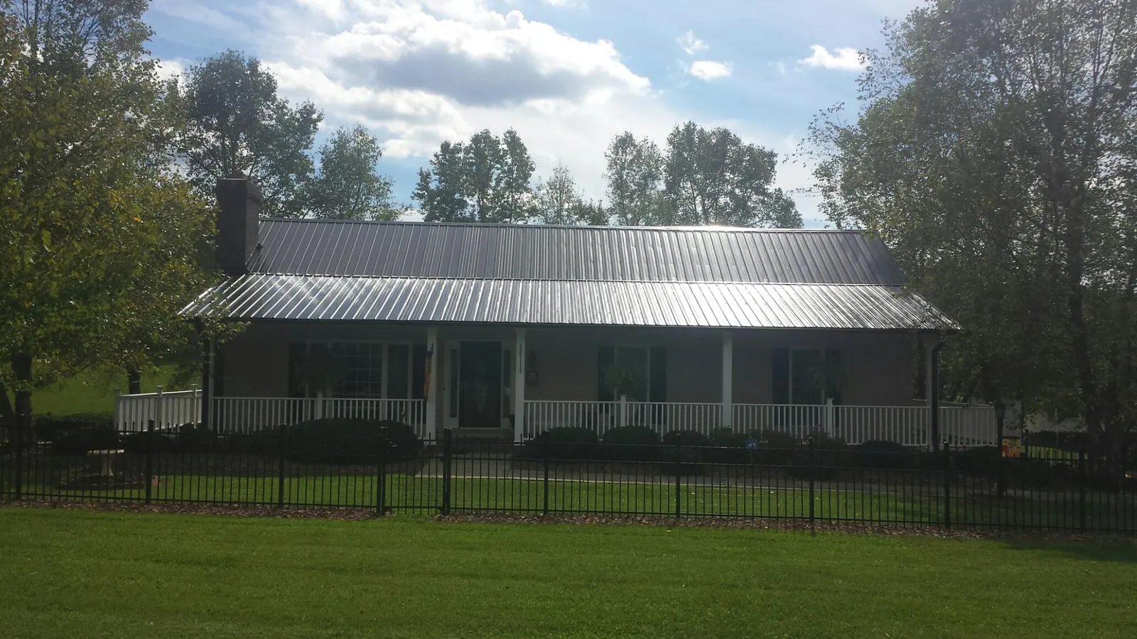 Gray metal roof on a brick ranch with a full width front porch — Gutter Guard Installation work by our crew in Saint Ann