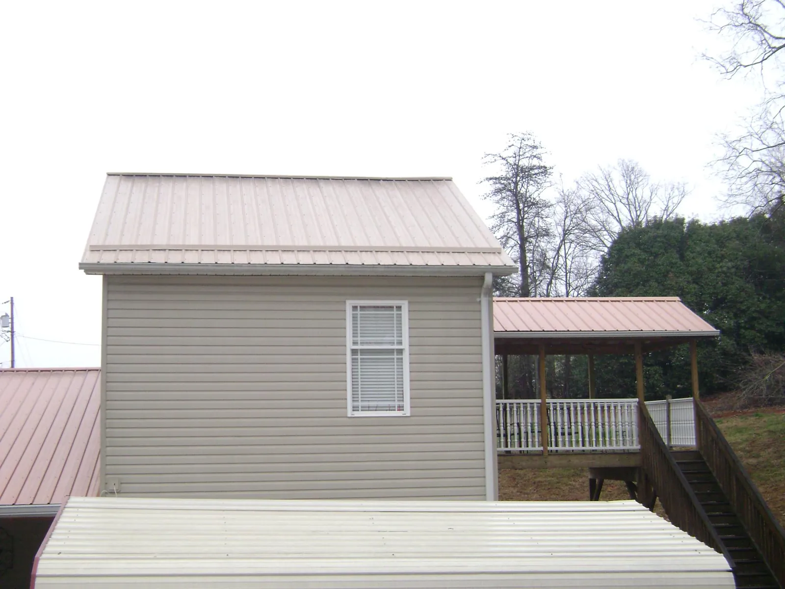 Tan metal roofs on a two story addition and attached porch, from a Roof Replacement job in Saint Ann